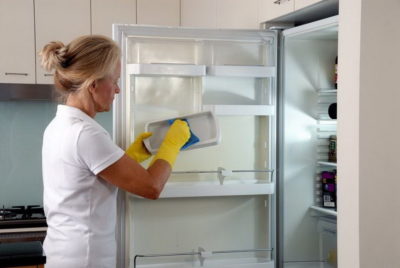 Женщина удаляет лед из холодильника